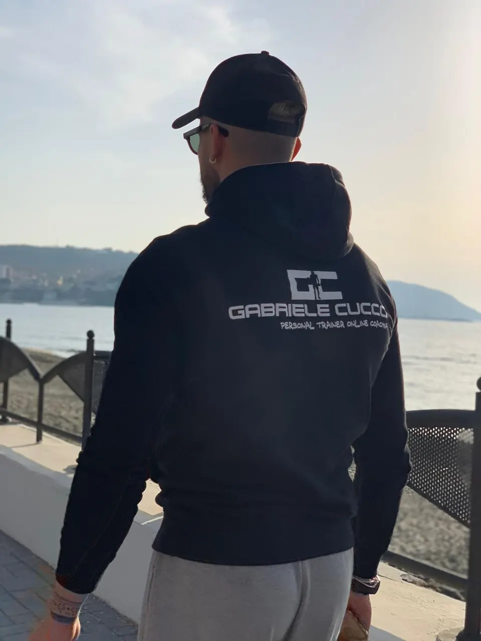 Gabriele Cucco di spalle in riva al mare con la felpa Personal Trainer Online Coaching